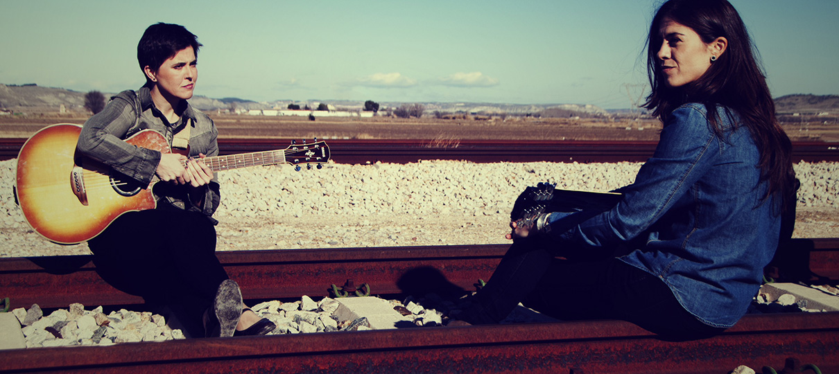 Ana y Susana sentadas sobre las vías del tren en la meseta, una de ellas con una guitarra acústica